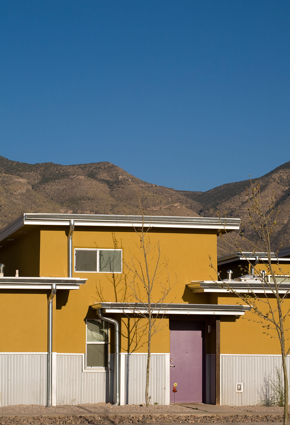 Two-story stucco apartment home with a colorful front door at Cottonwood Commons, foothills behind